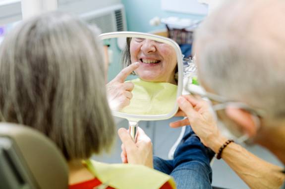 Patientin betrachtet Zähne im Spiegel